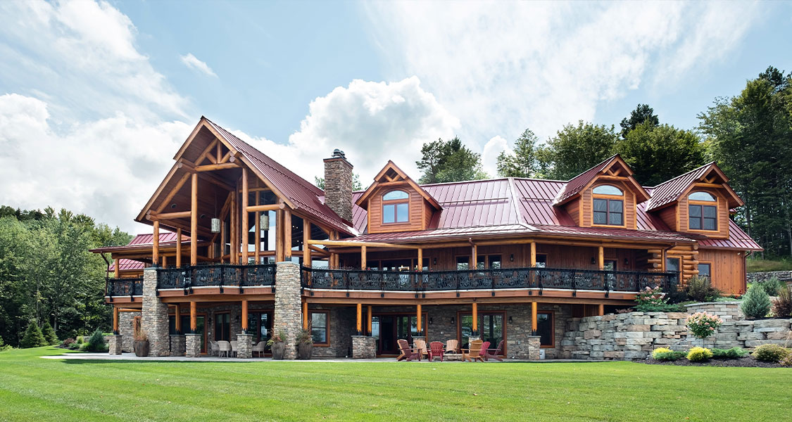 Custom Adirondack home with timber details, stone foundation, wraparound deck, and mountain views