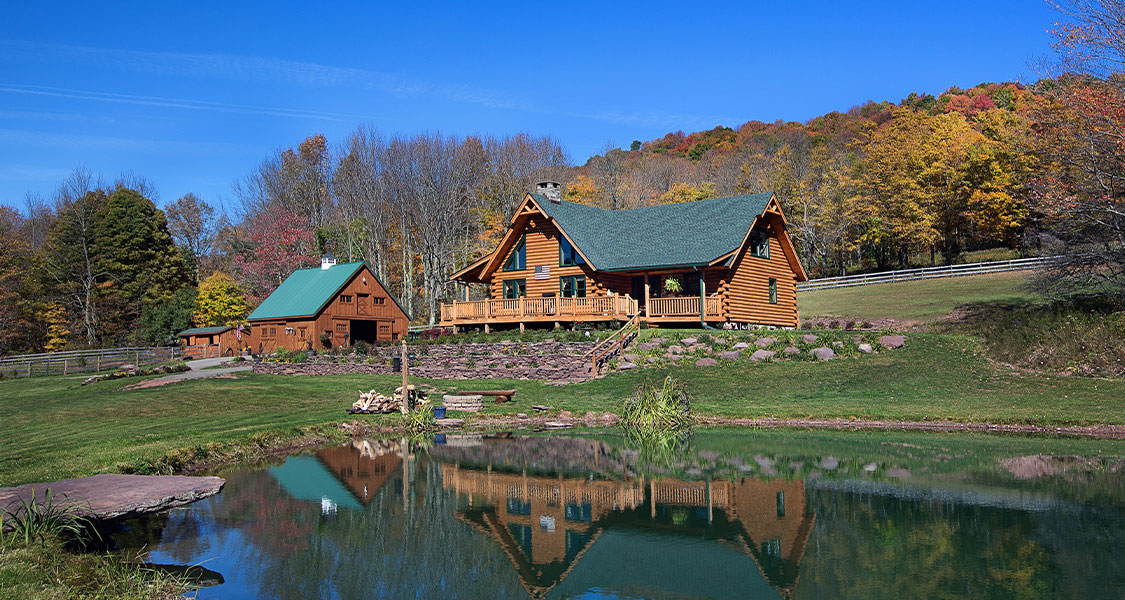 Traditional log home on a pond with a horse farm